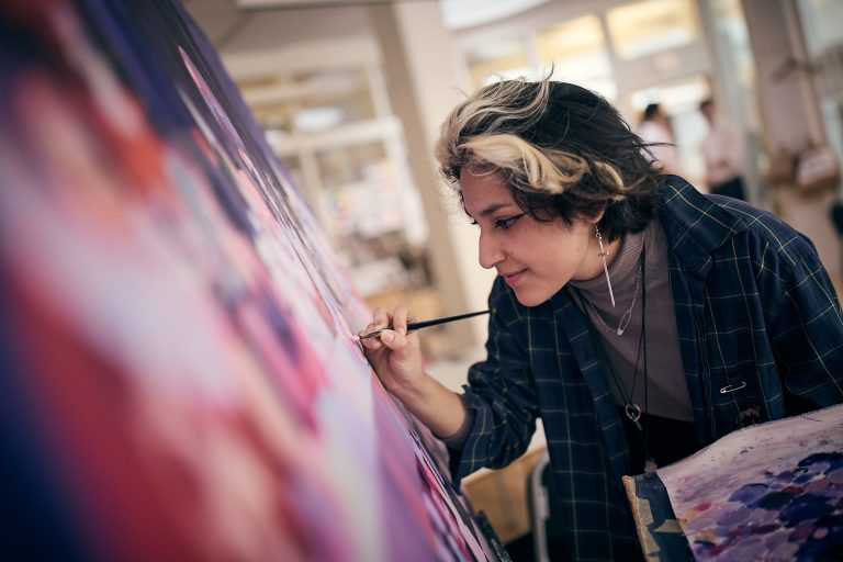 Elev med pensel mot en målarduk som målar på sitt gymnasiearbete.