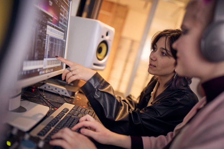 Två elever producerar musik framför en skärm.