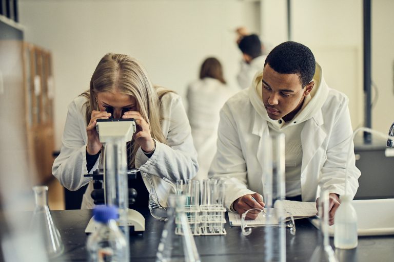 Elever studerar medicin i ett klassrum genom att titta i mikroskop.