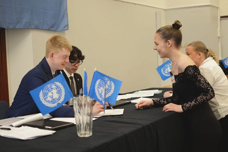 Fyra elever mittemot varandra vid ett bord med FN-flaggor. Eleverna deltar i FN-rollspel tillsammans.