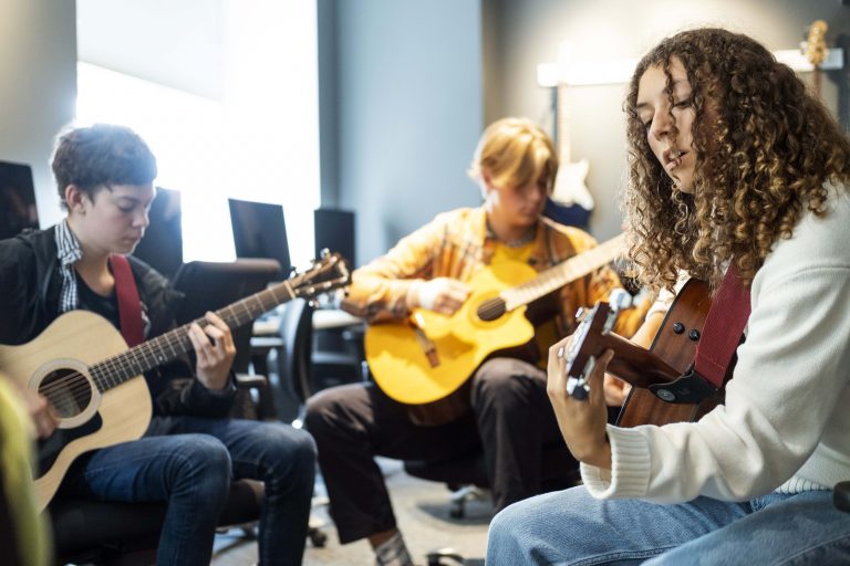 Tre elever musicerar tillsammans på gitarrer.