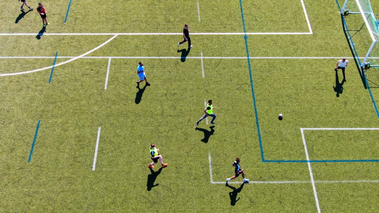 Några elever spelar fotboll på en fotbollsplan fotograferad ovanifrån.