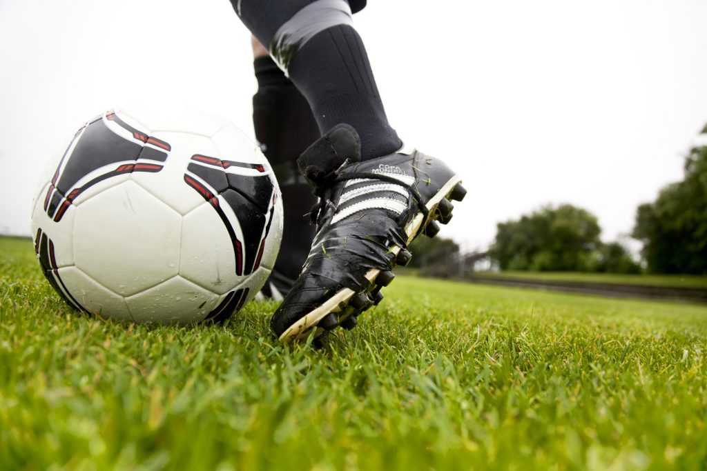 Fötter ,med fotbollsskor mot en fotboll på gräsmatta.