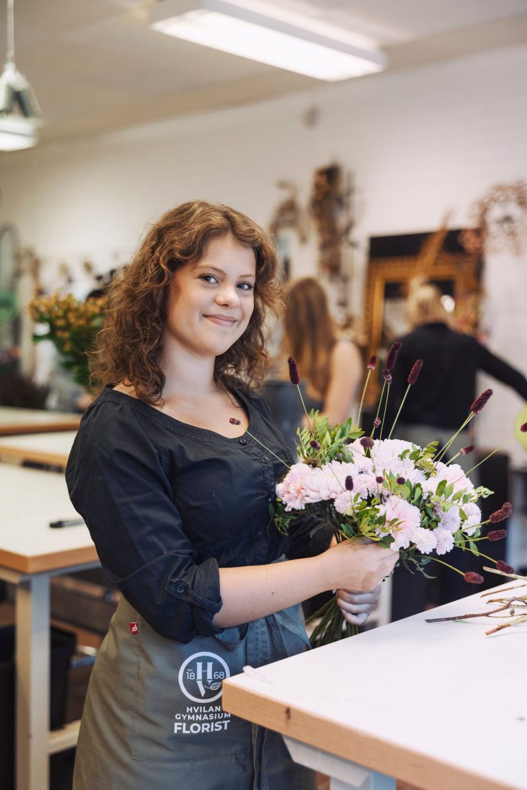En floristelev visar sin nygjorda bukett i floristklassrummet