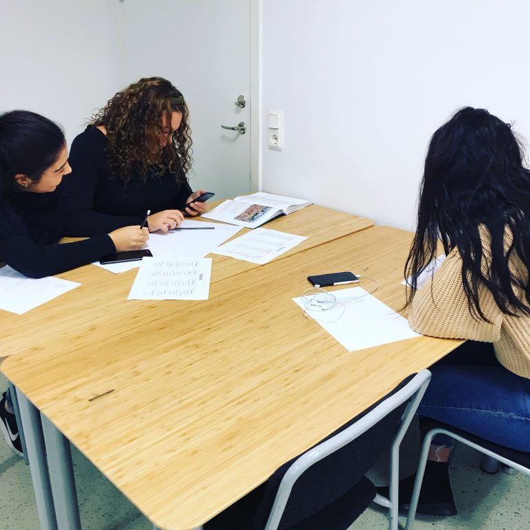 Tre elever sitter och studerar tillsammans vid ett bord med papper framför sig.