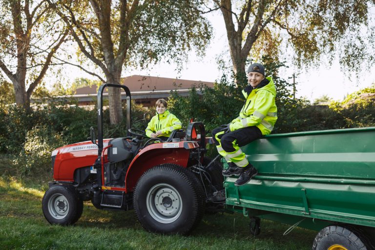 Två elever arbetar med traktor och släp i trädgårdsmiljö