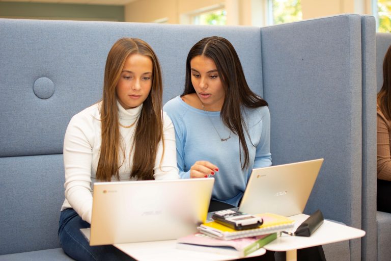 Två elever sitter och samarbetar framför två laptoppar i skolans lärcentrum.