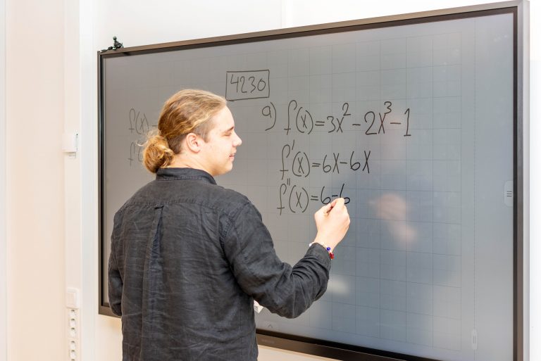 Teknikelev står framme och skriver på vita tavlan under en matematiklektion.