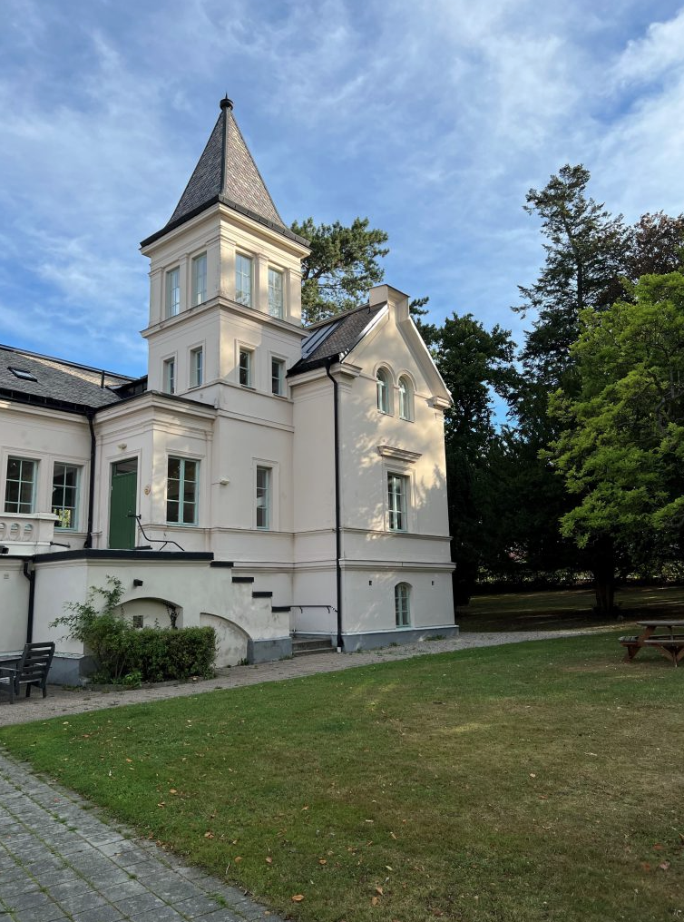 Vit byggnad med gräs och träd runtom. Quennerstedtska villan. En av skolans två fint belägen i Quennerstedska parken.