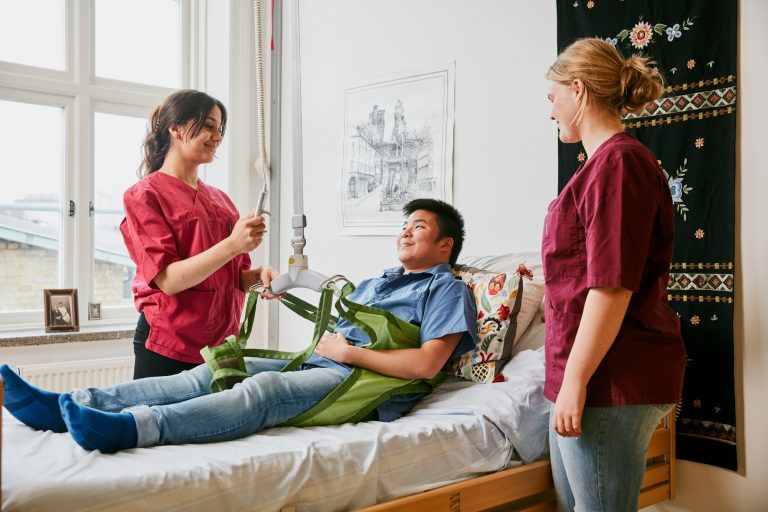 Tre elever övar praktiska moment på vård- och omsorgsprogrammet. En elev får agera som patient i en säng.