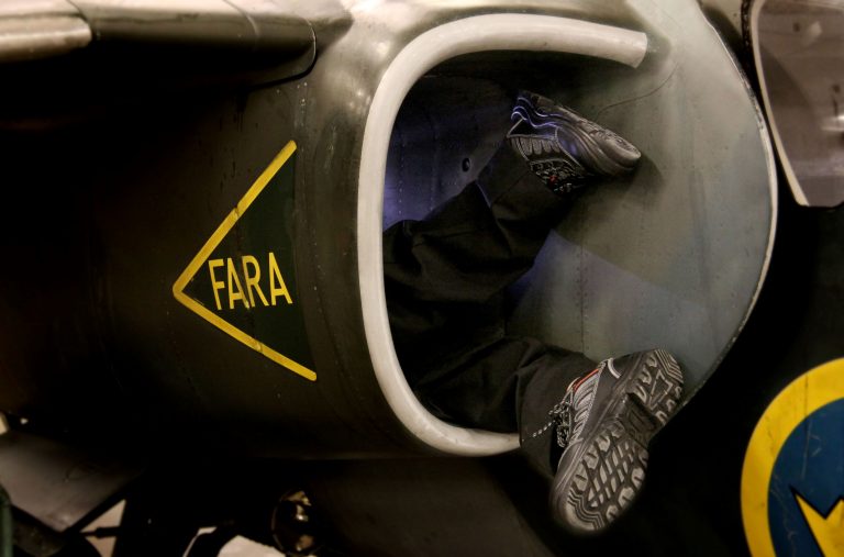 Två fötter sticker ut från ett luftintag på ett stridsflygplan där inspektion genomförs.