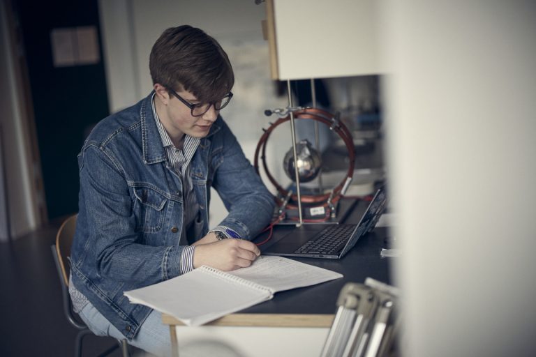 En elev i labbsalsmiljö gör anteckningar i en skrivblock.