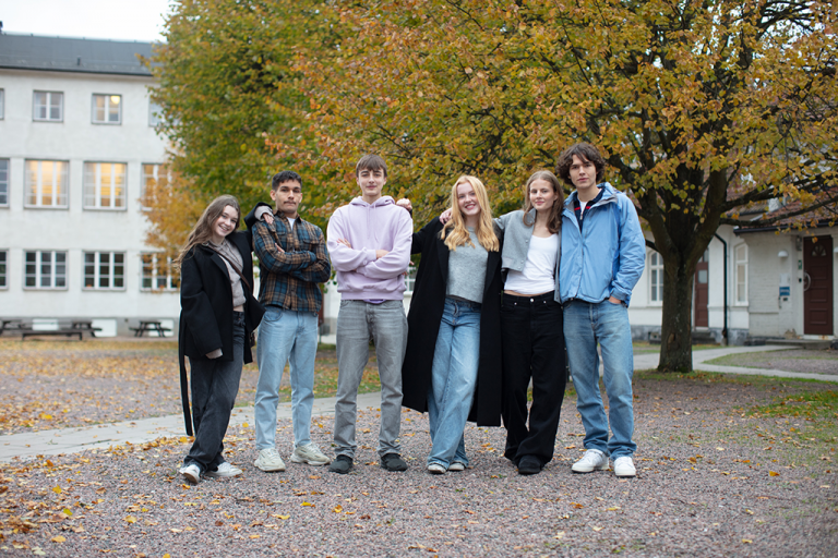 Sex stycken glada elever på skolans mysiga innergård.